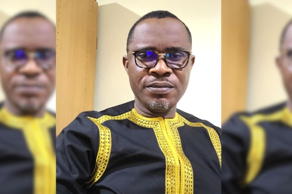 Portrait of Ezenwa Opara, a shaven haired black man with glasses and a goatee beard wearing a navy top with gold embroidery